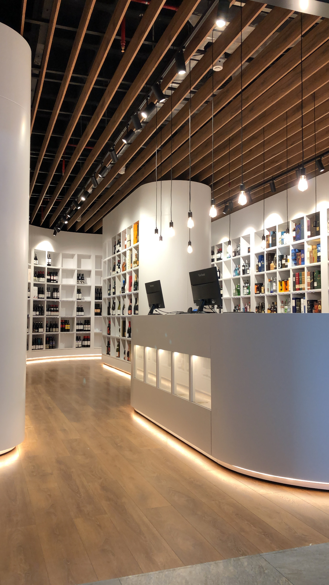 Aisle between wine shelves with the counter to one side and warm light at floor level