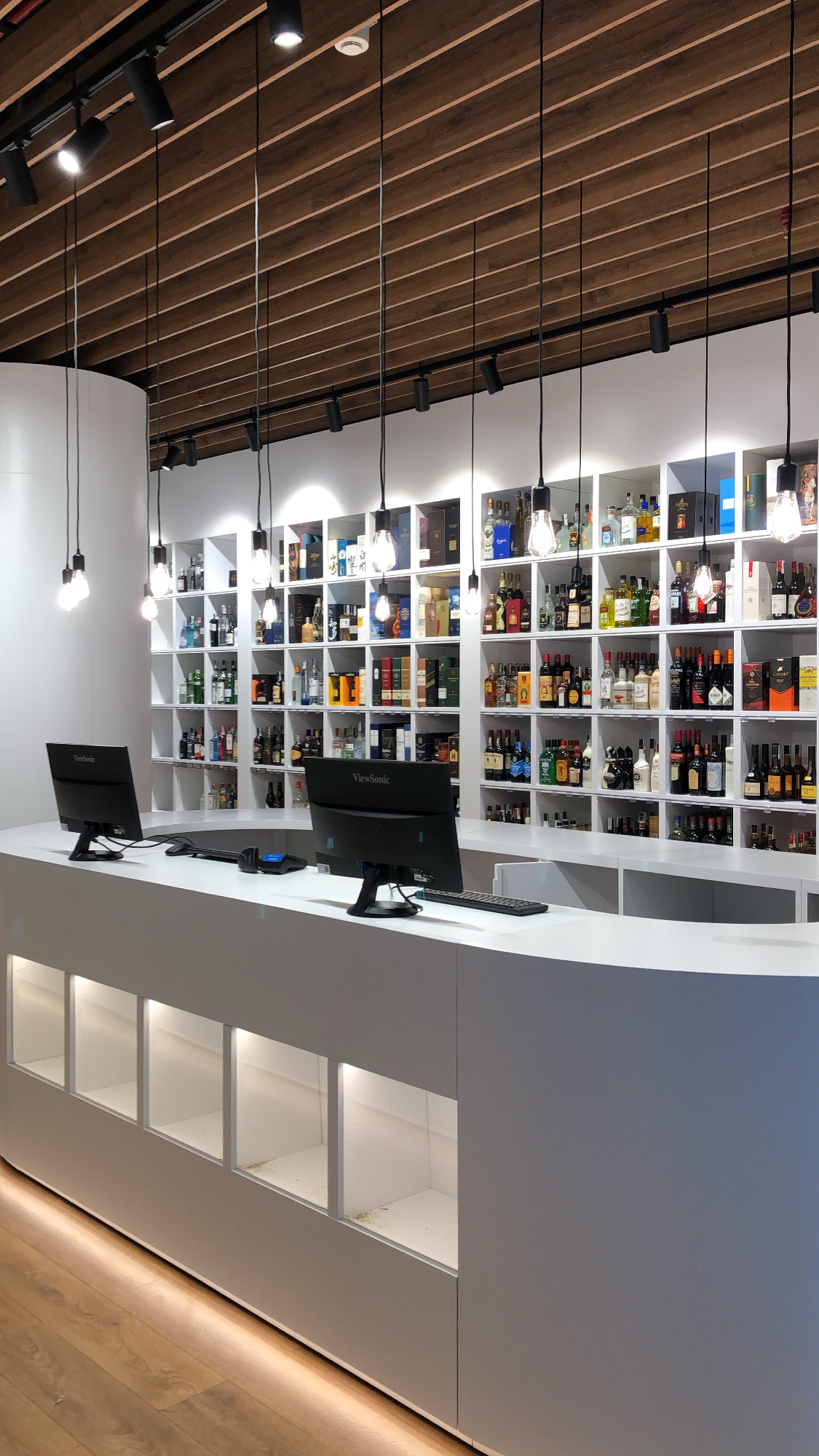 White oval counter with lit recesses in front of spirits shelving beneath hanging bulbs