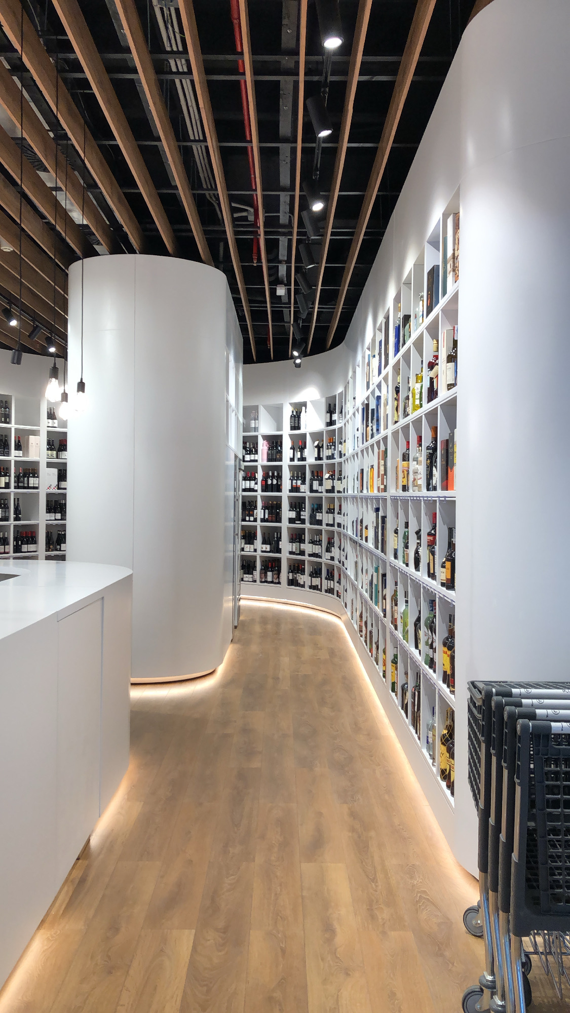 Curved aisle with spirits shelving and a timber floor lit along its edge