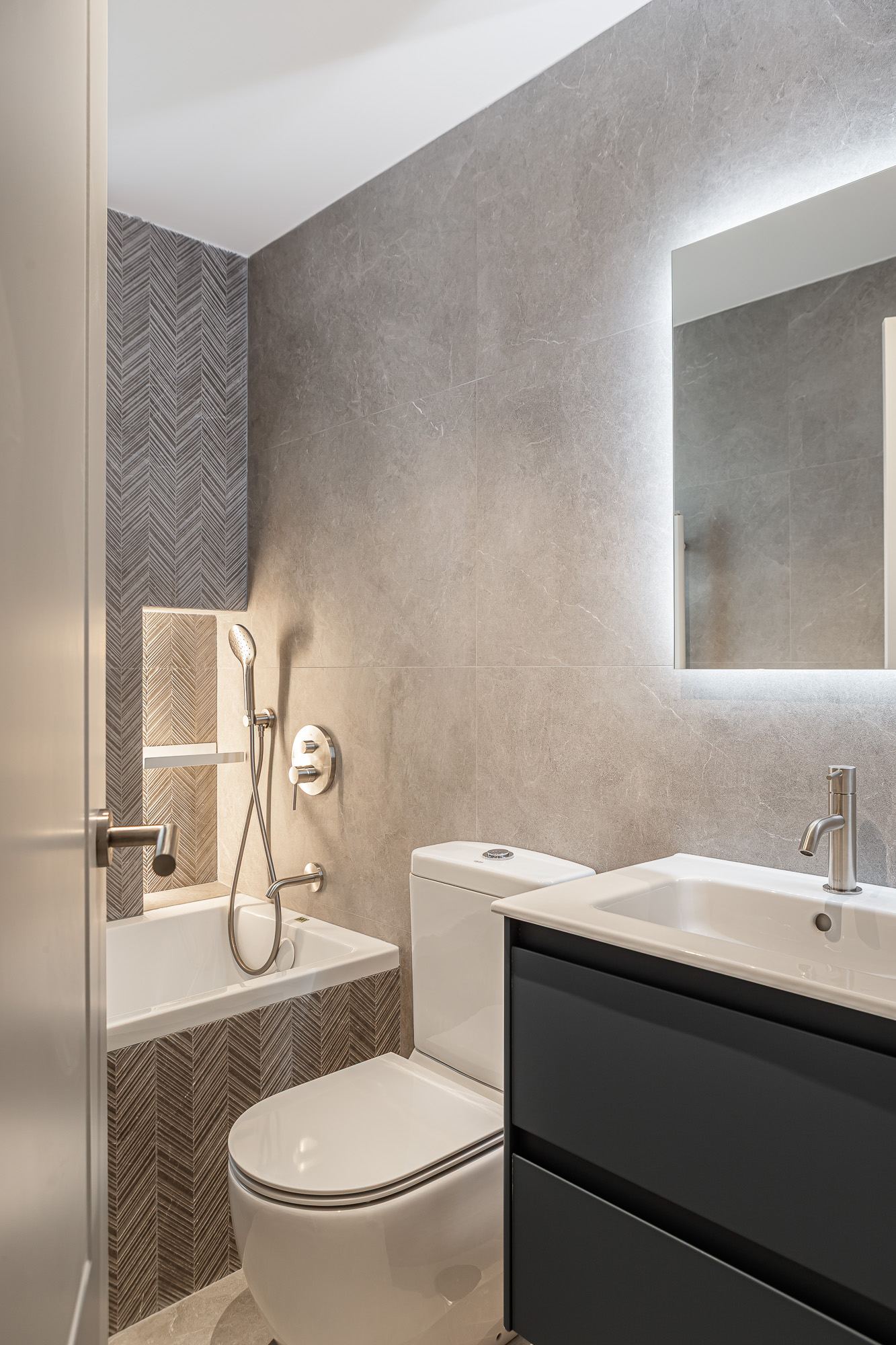 Bathroom with bathtub, herringbone-tiled niche, toilet and backlit mirror