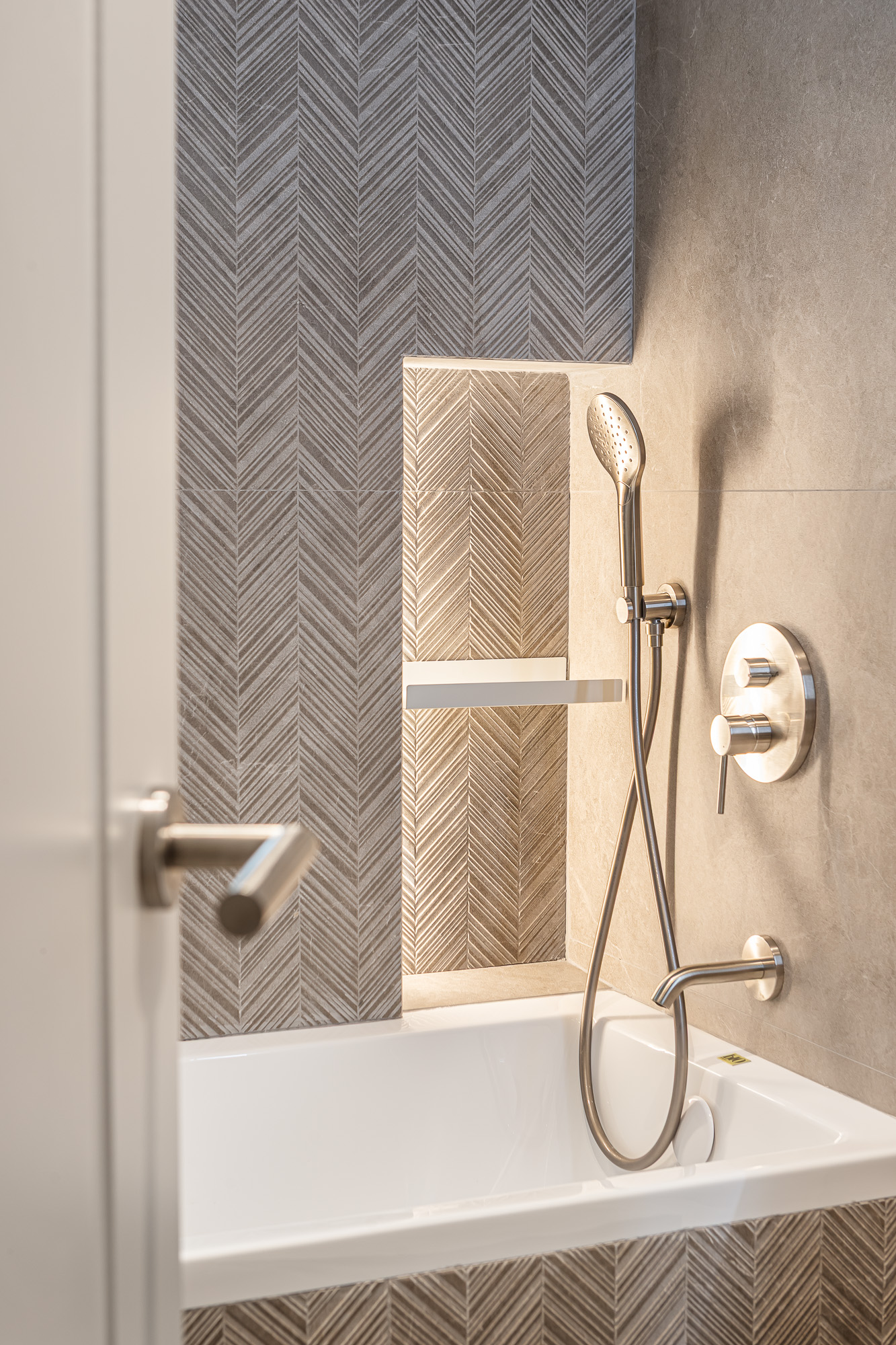 Detail of the bathtub area with a herringbone-tiled niche and wall-mounted shower fittings