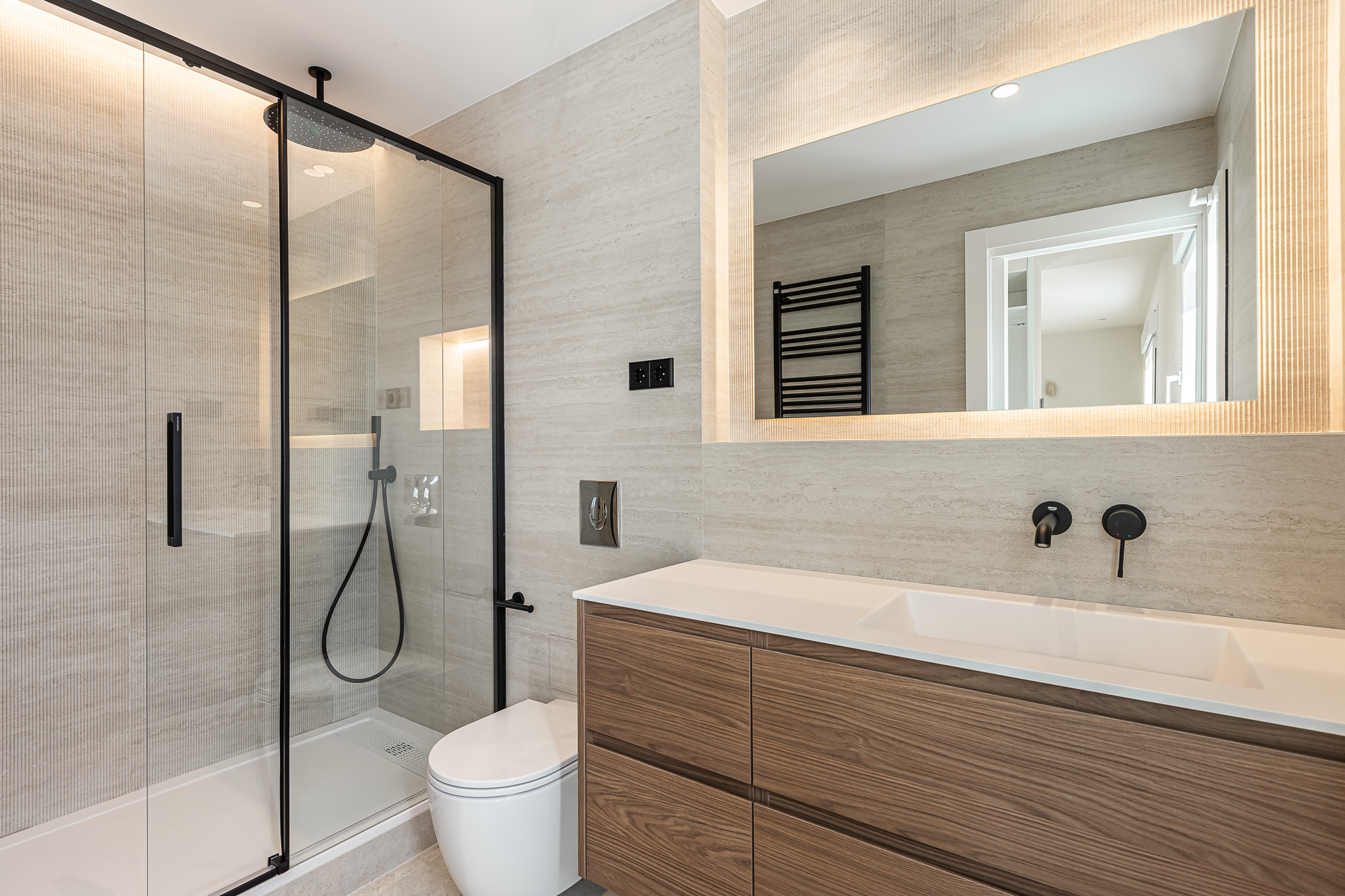 Bathroom with a black-framed glass shower screen, wood vanity and backlit mirror