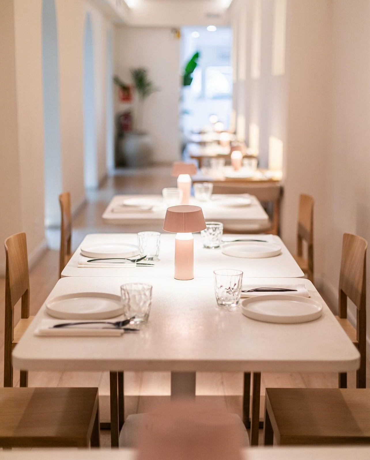 Row of white tables with portable lamps in a long, light-toned dining room