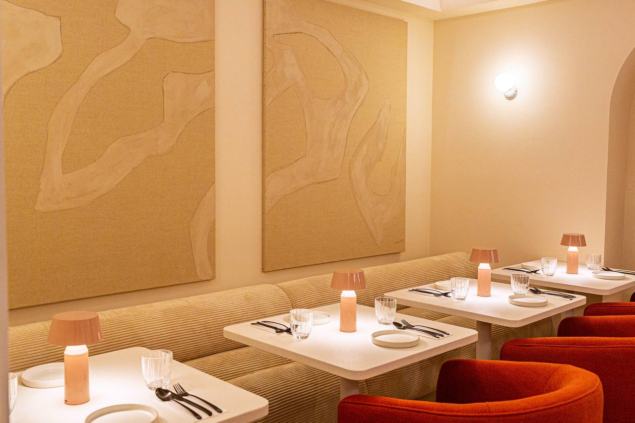 Beige corduroy banquette beneath two textured canvas panels, with white tables and red armchairs
