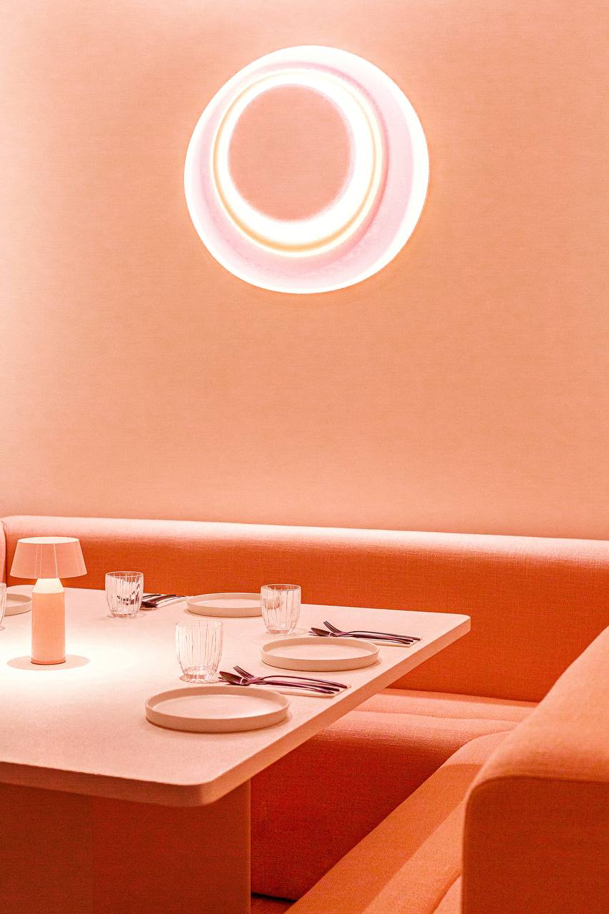 Glowing circular light fitting above an orange banquette and a laid table