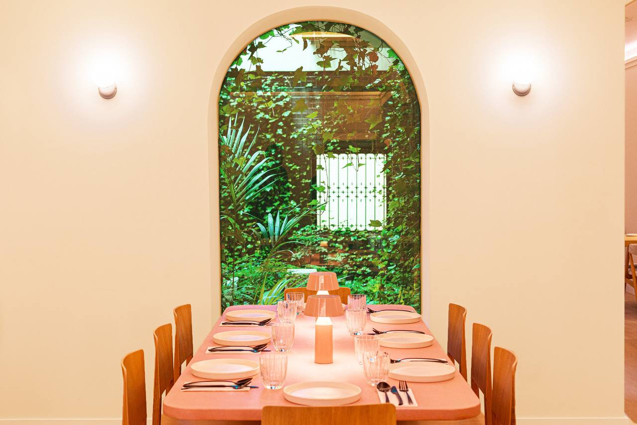 Long dining table facing an arch that frames an interior courtyard covered in ivy — Mudrá Restaurant