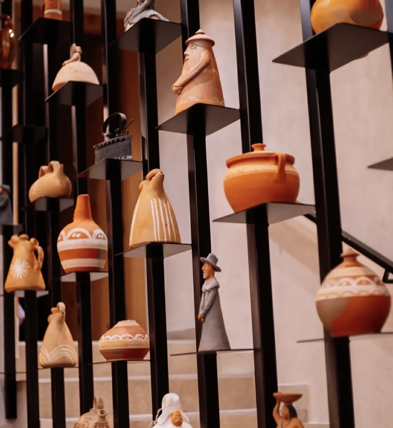 Detail of ceramic pieces and clay figures on black metal shelves beside the staircase