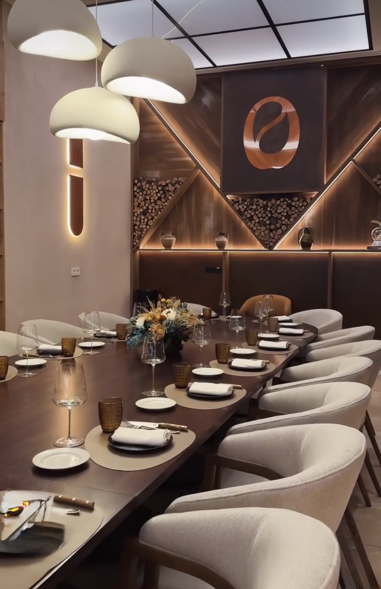 Detail of the laid table with wine glasses, amber tumblers and dried flowers, with the lit wood wall behind
