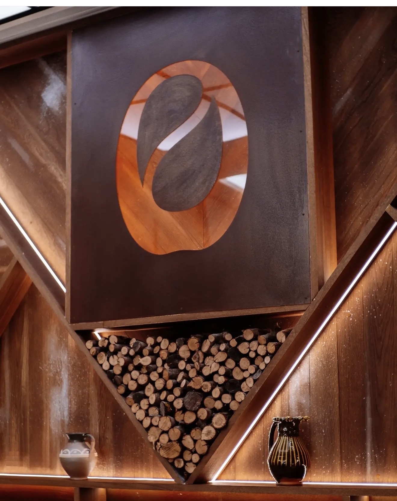 Detail of a panel with a cut-out oval emblem and a triangular niche of stacked firewood, between lines of light