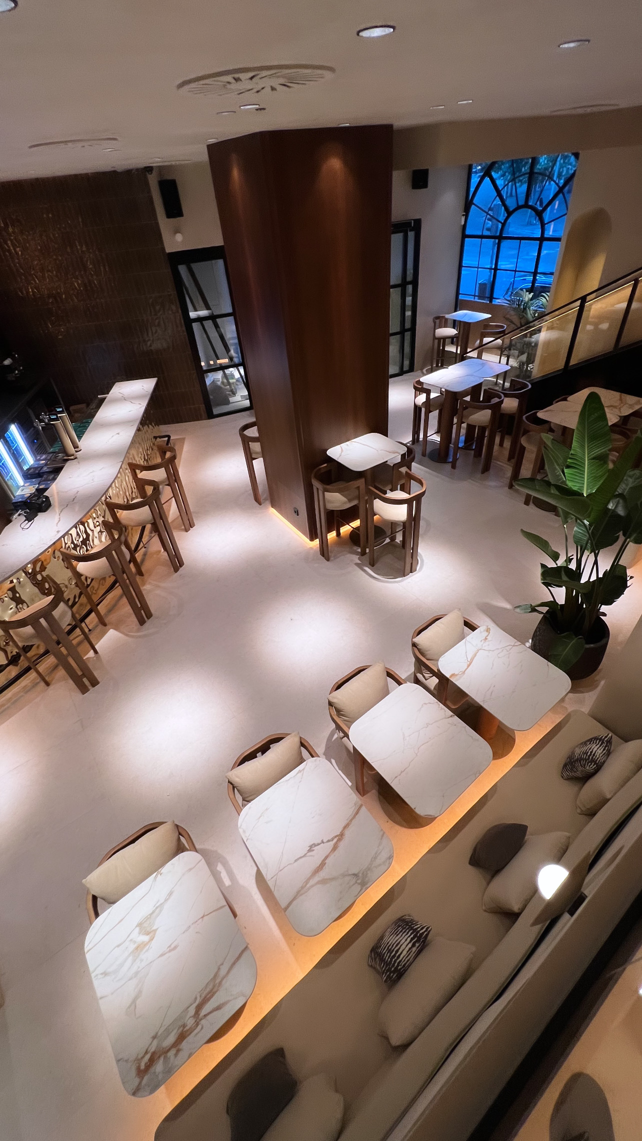 View from above of the dining room with a curved bar with a veined top, a timber-clad column and an arched window