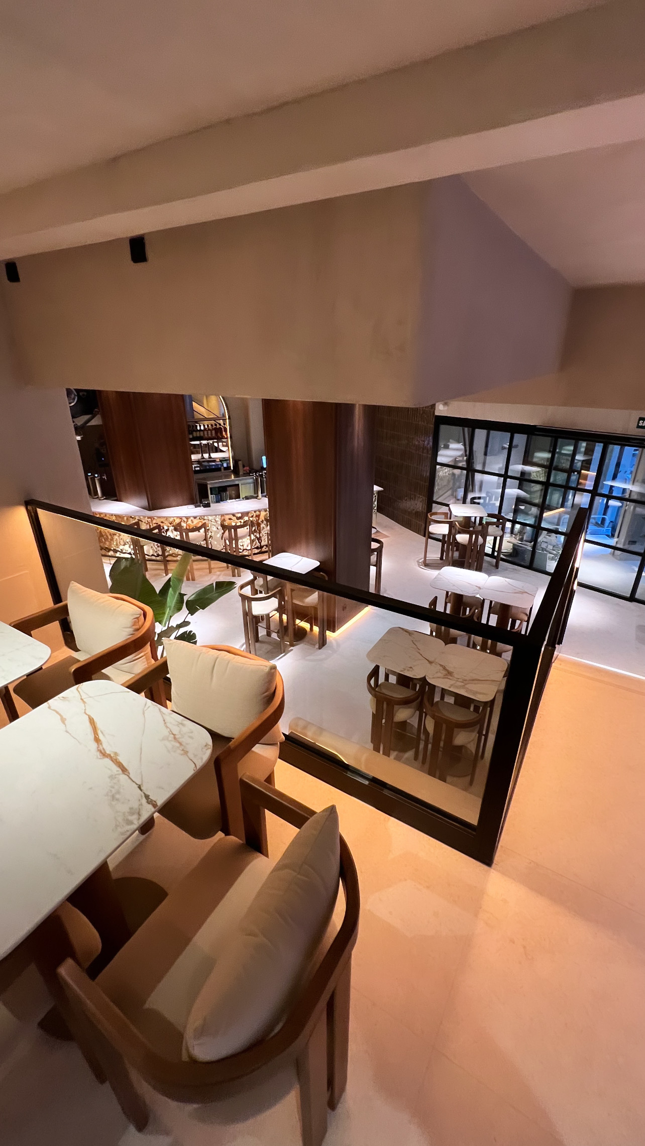 View from an upper level, through a glass balustrade, of the bar and the lower dining room with a glazed door