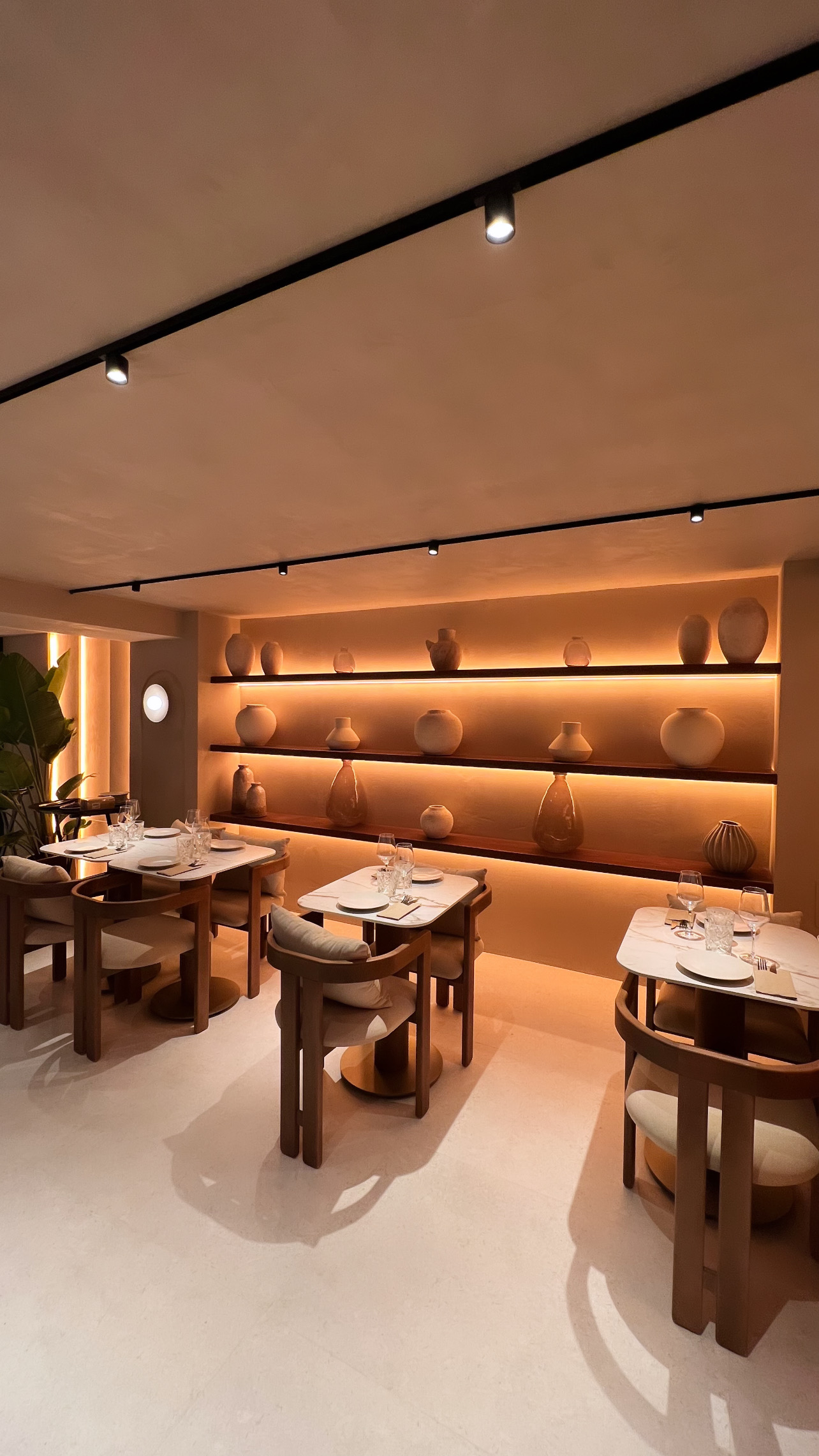 Timber shelving with ceramic vases under indirect light, beside tables with veined tops